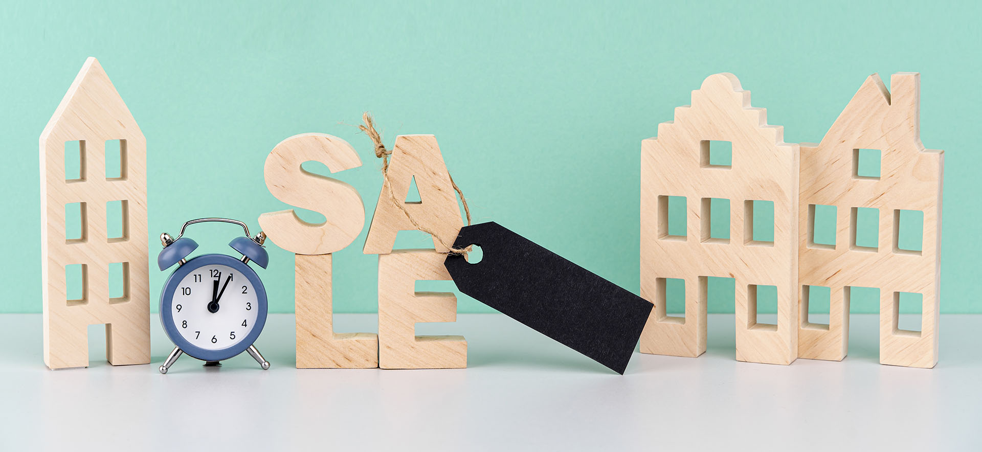 Kleine Modellhäuser aus Holz und ein Sale-Schild repräsentieren den Ablauf beim Immobilienkauf