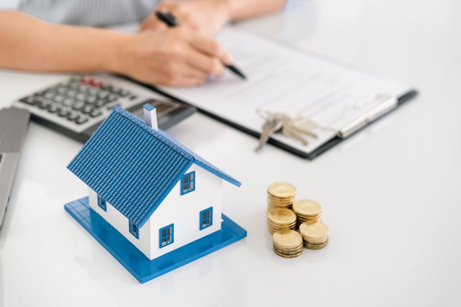 Mensch sitzt über einem Bewertungsbogen für Immobilien, daneben liegt ein Taschenrechner und ein kleines Häuschen mit einem Stapel Münzen